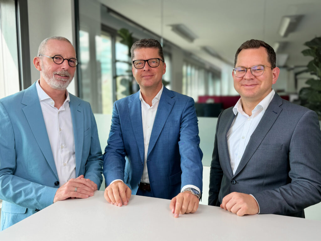 Drei Personen in Businesskleidung an einem Besprechungstisch in einem modernen Büro.